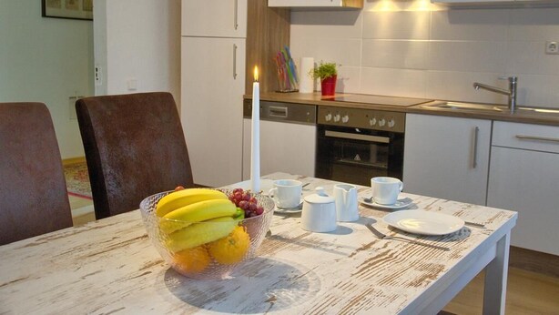 Een moderne keuken met witte kasten, een eettafel met een schaal fruit en een brandende kaars.