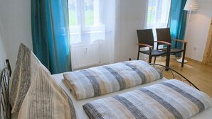 Een slaapkamer met een bed, twee stoelen, een lamp en een raam met gordijnen.