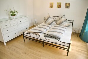 Un dormitorio con una cama, un aparador, una mesita de noche con lámpara y una planta en maceta.