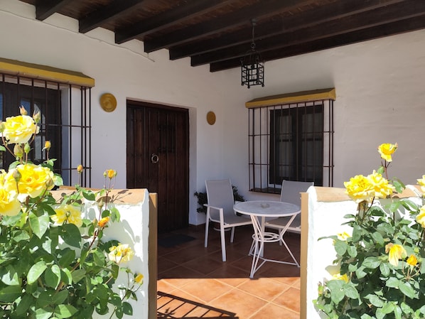 Un espace patio avec une table et des chaises, une porte et des rosiers jaunes.