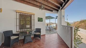 Um pátio com móveis de vime, uma mesa de vidro e vista para o campo.