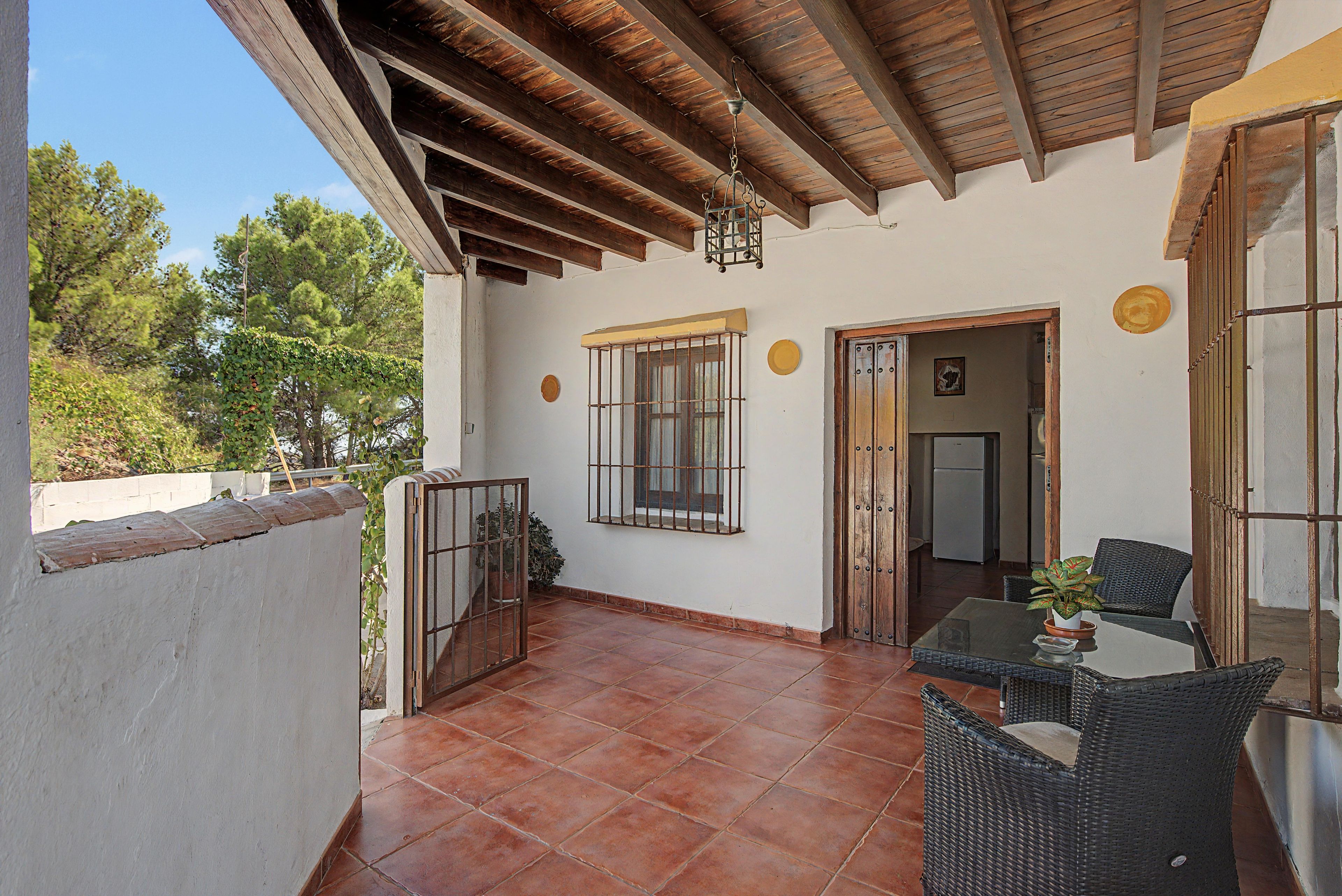 A covered patio with a tiled floor, a table with chairs, a hanging light fixture, and a door leading to an interior space.