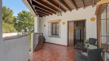 A covered patio with a tiled floor, a table with chairs, a hanging light fixture, and a door leading to an interior space.