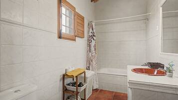 A bathroom with white tiled walls, a wooden shelf with baskets, a white bathtub, and a wooden window with shutters.