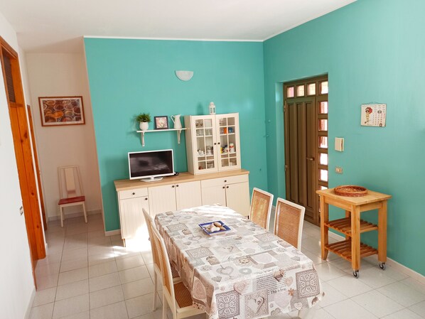 A dining area with a table set for two, a television on a cabinet, and a calendar on the wall. - Apartment in villa facing the sea - Green Apartment (Torino di Sangro)