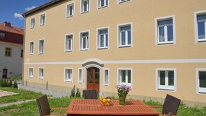 A two-story building with a flat roof, a central entrance, and a small garden area with a wooden table and chairs. - Dresdner-Tag Helene (Dresden)
