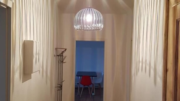 A hallway with a patterned ceiling, a hanging light fixture, a red chair, and a table in the background. - Dresdner-Tag Helene (Dresden)