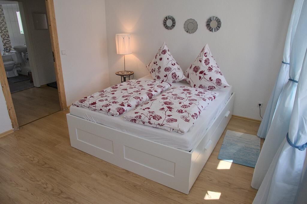 A bedroom with a white bed, floral bedding, a bedside lamp, and a view of the bathroom.