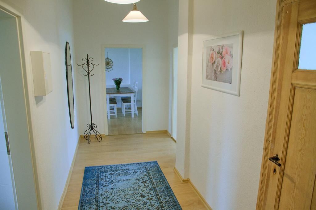 A hallway with a wooden floor, a blue patterned rug, a white door, and a framed picture on the wall.