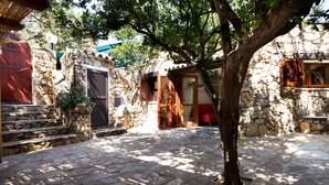 Un edificio de piedra con una escalera de madera, un árbol en primer plano y una puerta roja.