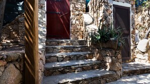 Una escalera de piedra que conduce a una puerta roja, con un poste de madera y una planta en maceta a la derecha.