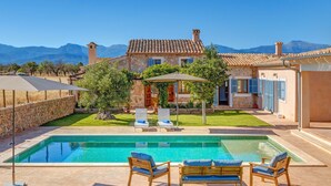 Una casa de pedra amb piscina, mobiliari exterior i muntanyes al fons.