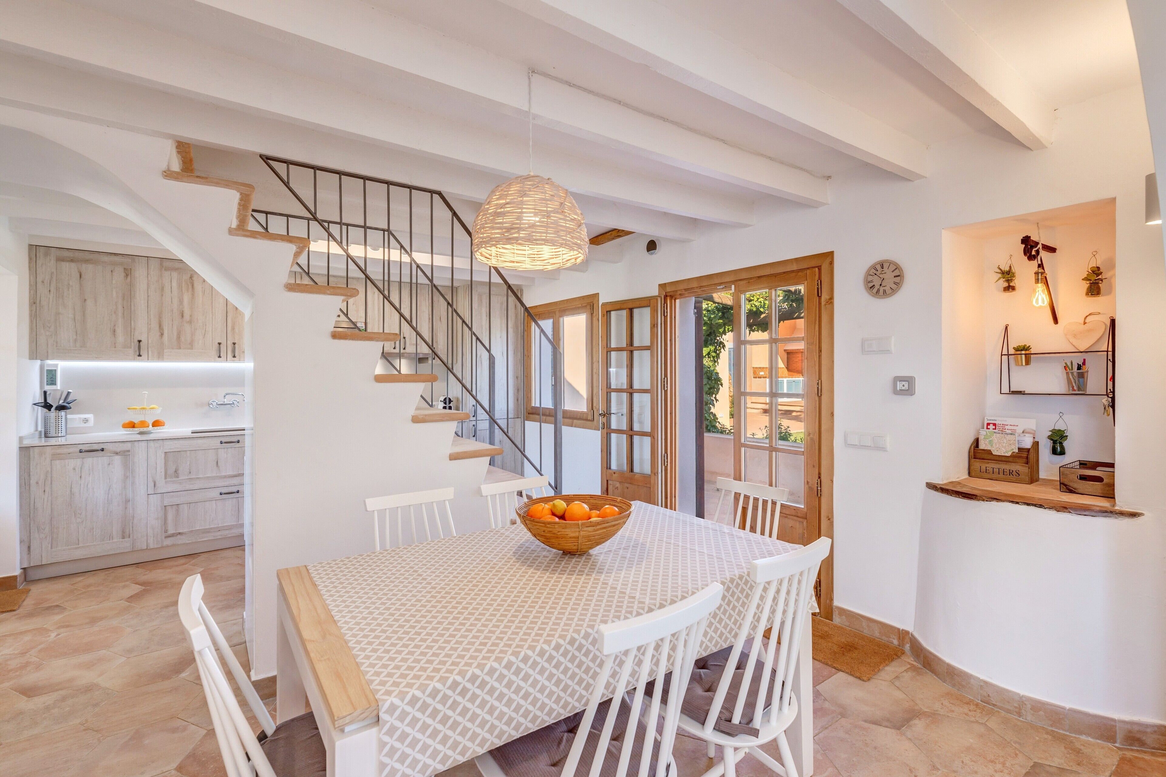 A modern kitchen with white cabinets, a wooden staircase, and a dining area with a table and chairs.