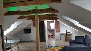 Un loft amplio con techo alto, vigas de madera a la vista, una zona de comedor, una sala de estar con sofá y una cocina.