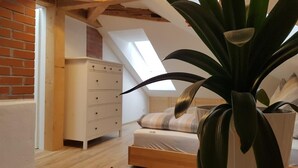 A bedroom with a sloped ceiling, a white dresser, a bed with a striped pillow, and a large plant. - Dresdner-Tag Hermann (Dresden)