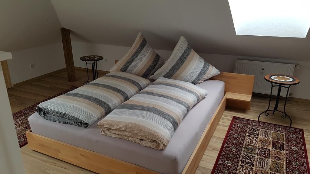 A bedroom with a bed, a small table, a radiator, and a window.