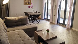 A modern living room with a sofa, a coffee table, a dining table with chairs, and a painting on the wall.