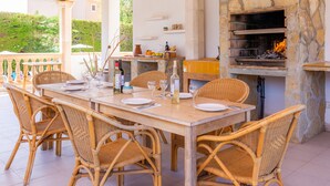 Un espace extérieur aménagé pour les repas, avec des chaises en osier et une cheminée en pierre.