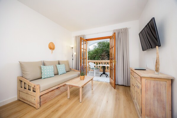 A room with a wooden sofa, a small wooden table, a TV on a wooden cabinet, and an open door leading to an outdoor area with a table and chairs.