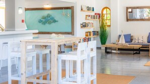 Un intérieur moderne avec une table à manger en bois, des chaises blanches, une bibliothèque et un coin salon confortable avec un canapé et des coussins.