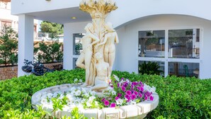 Un bâtiment blanc doté d’un balcon, une statue placée dans un jardinière circulaire et une moto garée à l  ’extérieur.