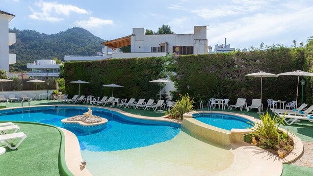 Une piscine entourée de verdure et de bâtiments, avec des chaises longues et des parasols.