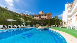 A swimming pool with lounge chairs and umbrellas, surrounded by greenery and buildings. - Apartment Close to the Beach with Pool Access, Private Terrace, Air Conditioning and Wi-Fi (Canyamel)