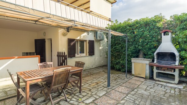 An outdoor patio with a wooden table and chairs, a barbecue grill, and a covered seating area. - Studio near the beach - Apartment Lucia (Campo nell'Elba)