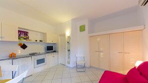 A modern kitchen with white cabinets, a dining area with a white chair, a red sofa, and a wardrobe with sliding doors. - Studio near the beach - Apartment Lucia (Campo nell'Elba)