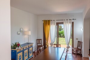 Un comedor con una larga mesa, sillas, un aparador con adornos y vistas a un jardín a través de una puerta.