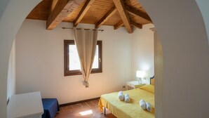 Ein Schlafzimmer mit einem Bett, einem Nachttisch, einer Lampe, einem Fenster mit Vorhängen und einer Holzbalkendecke.