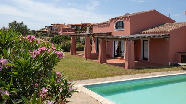 Ein Wohngebäude mit Swimmingpool, überdachter Terrasse und Garten mit rosa Blumen.