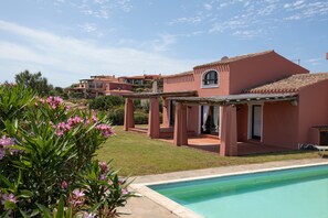 Un edificio residencial con piscina, un patio cubierto y un jardín con flores rosadas.