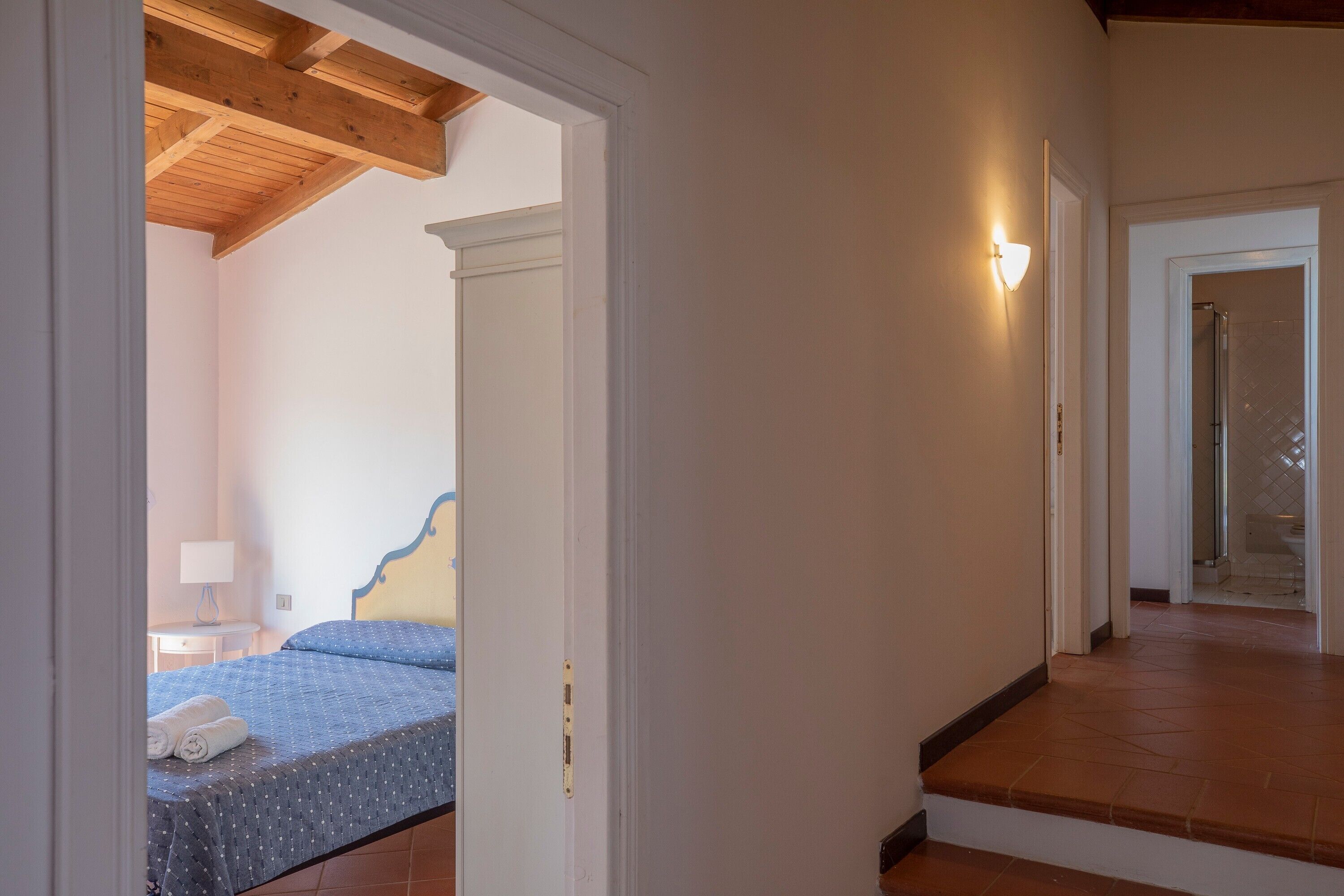 A bedroom with a bed, a nightstand, a lamp, and a bathroom visible through an open door.