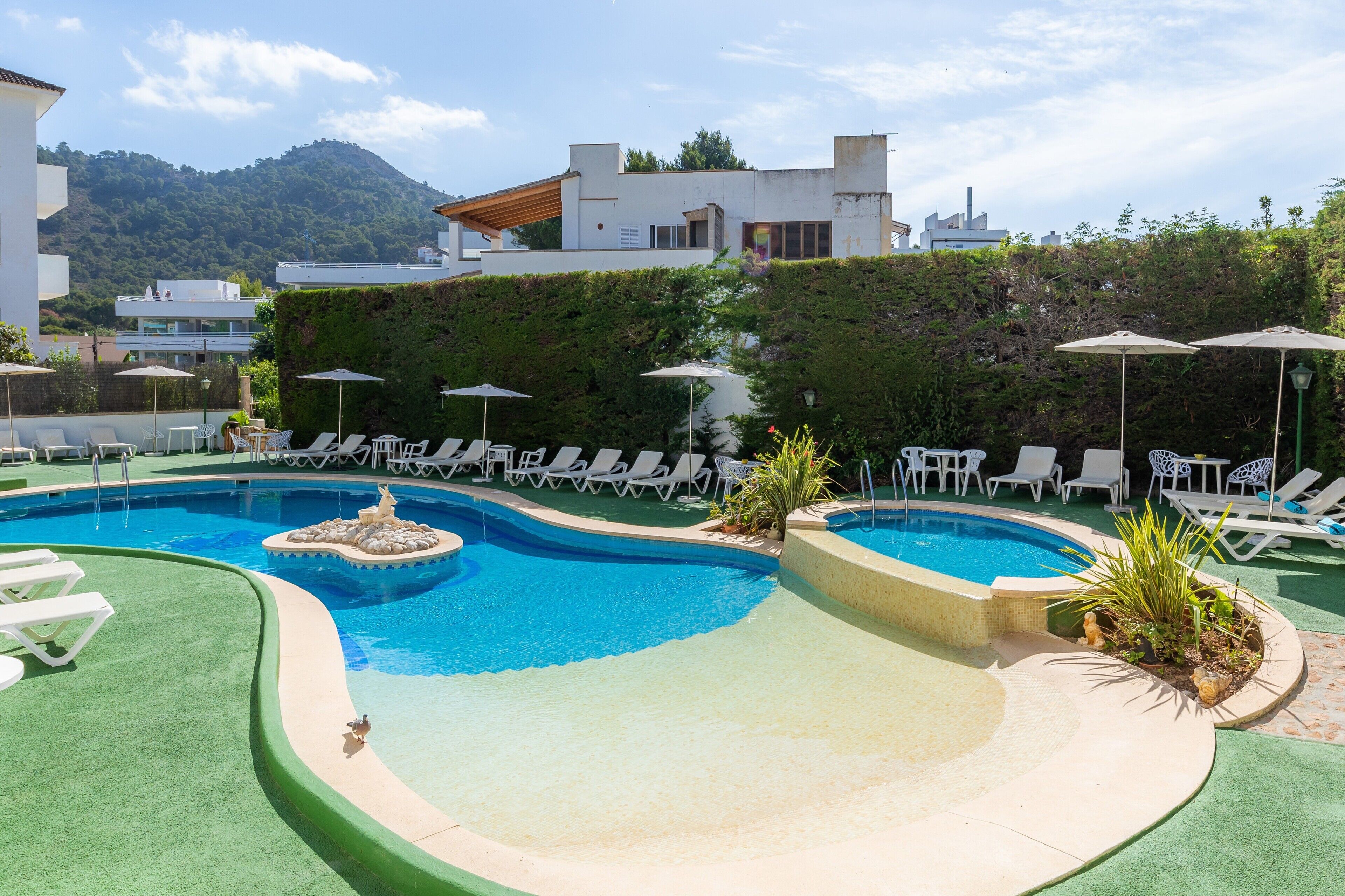 A pool area with lounge chairs, a small water feature, and a view of a hillside.