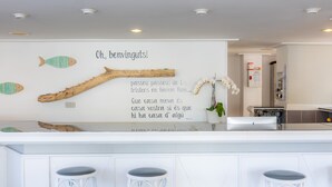 A modern kitchen with a white countertop, three bar stools, decorative fish wall art, a wooden branch, and a French quote. - Apartment Close to the Beach with Pool Access, Private Terrace, Air Conditioning and Wi-Fi (Canyamel)