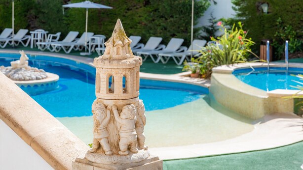 A pool area with lounge chairs, a decorative fountain, and a stone structure. - Apartment Close to the Beach with Pool Access, Private Terrace, Air Conditioning and Wi-Fi (Canyamel)
