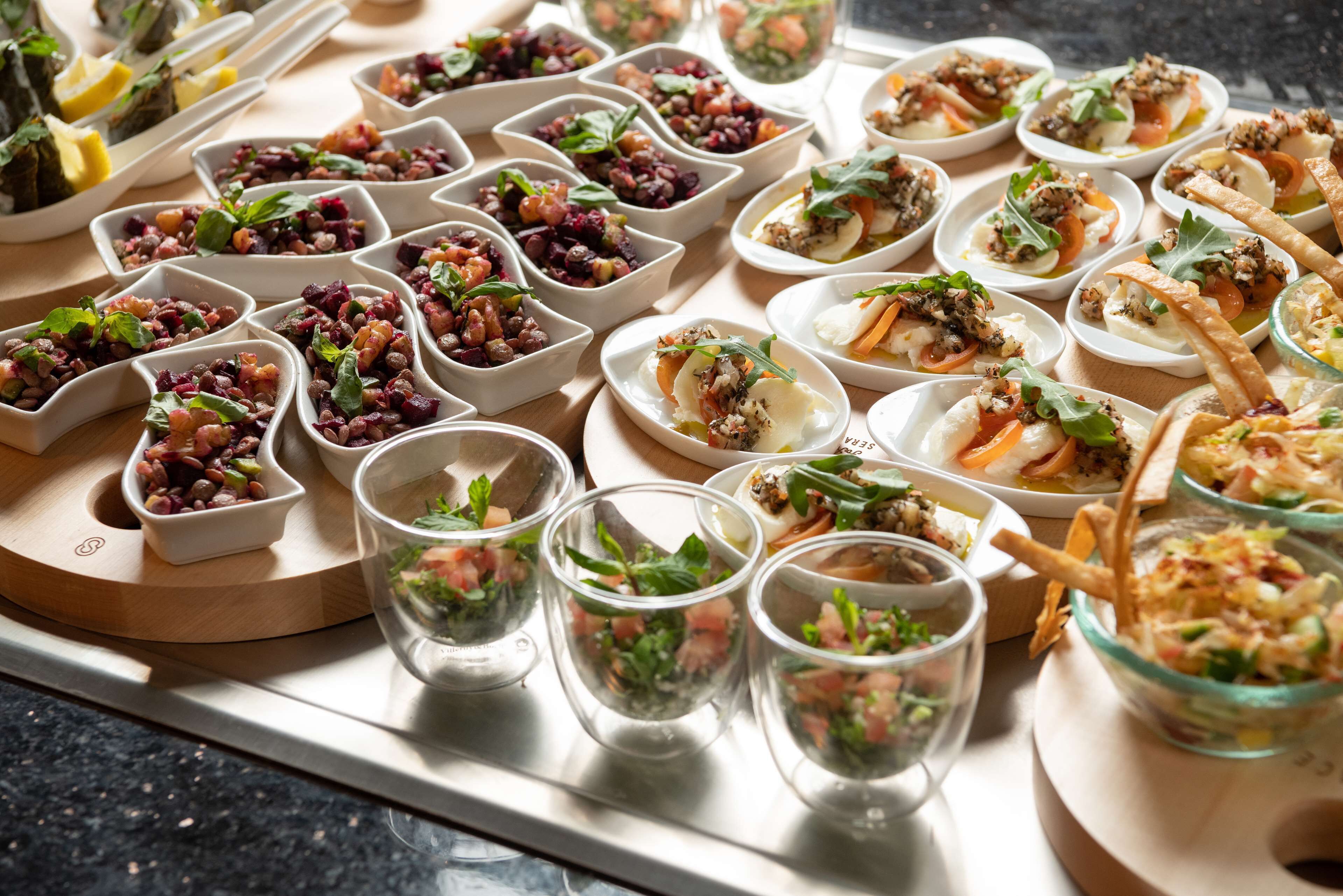 A variety of small dishes and glasses of food arranged on a wooden board.