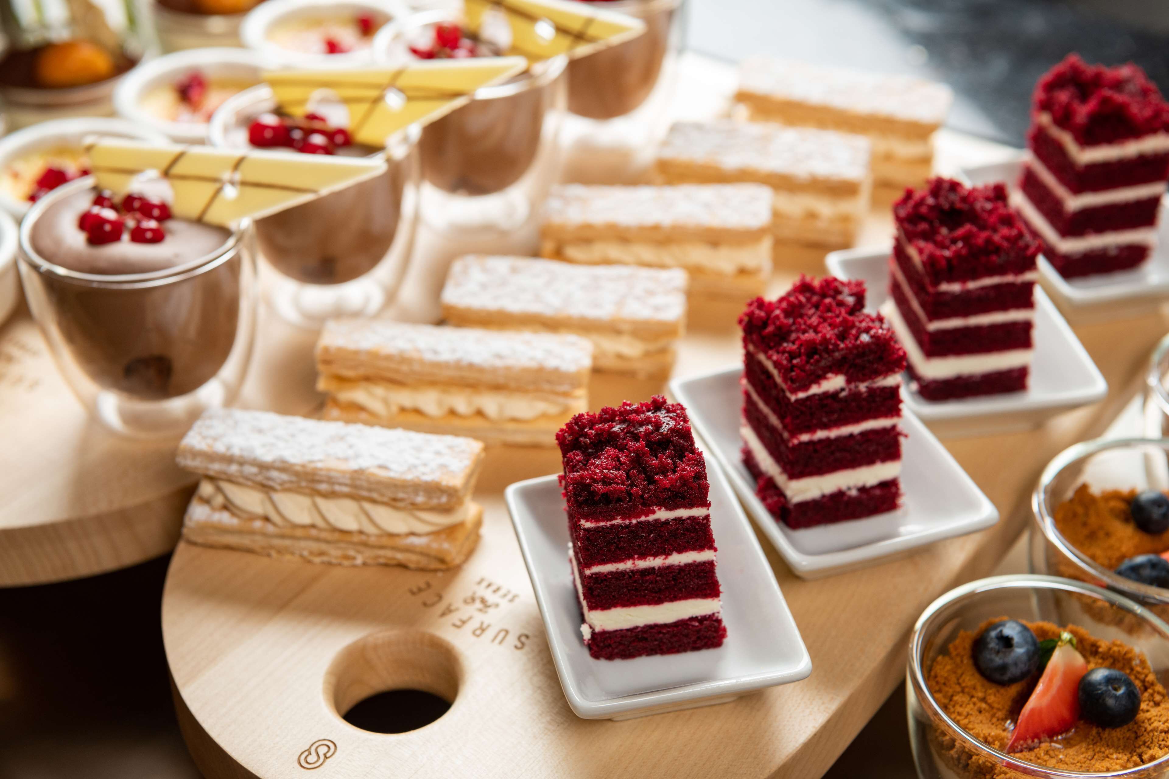A variety of desserts on a wooden board, including layered cakes and a chocolate dessert with berries.