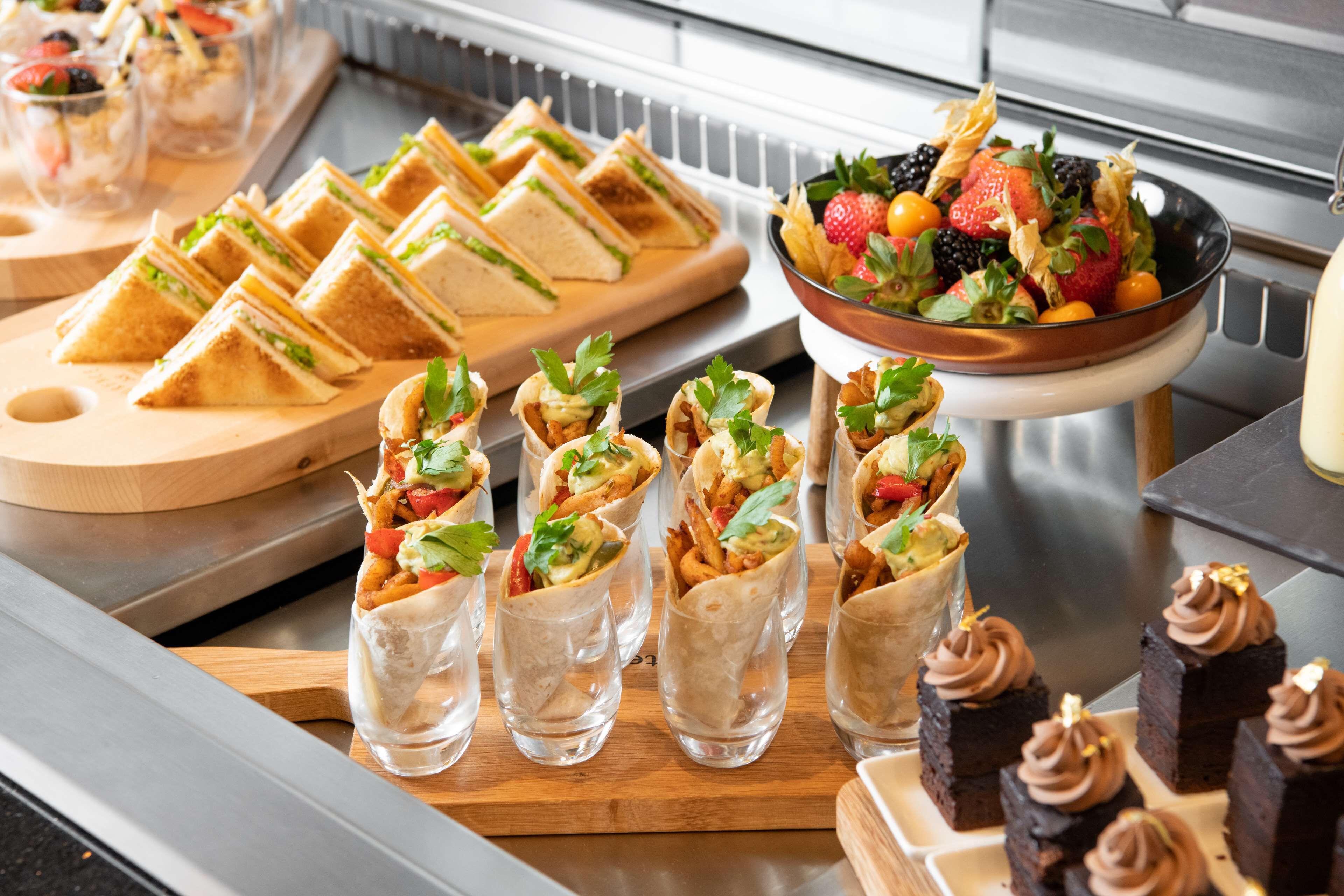 Un bufé con diversas opciones de comida, incluyendo sándwiches, wraps y postres.