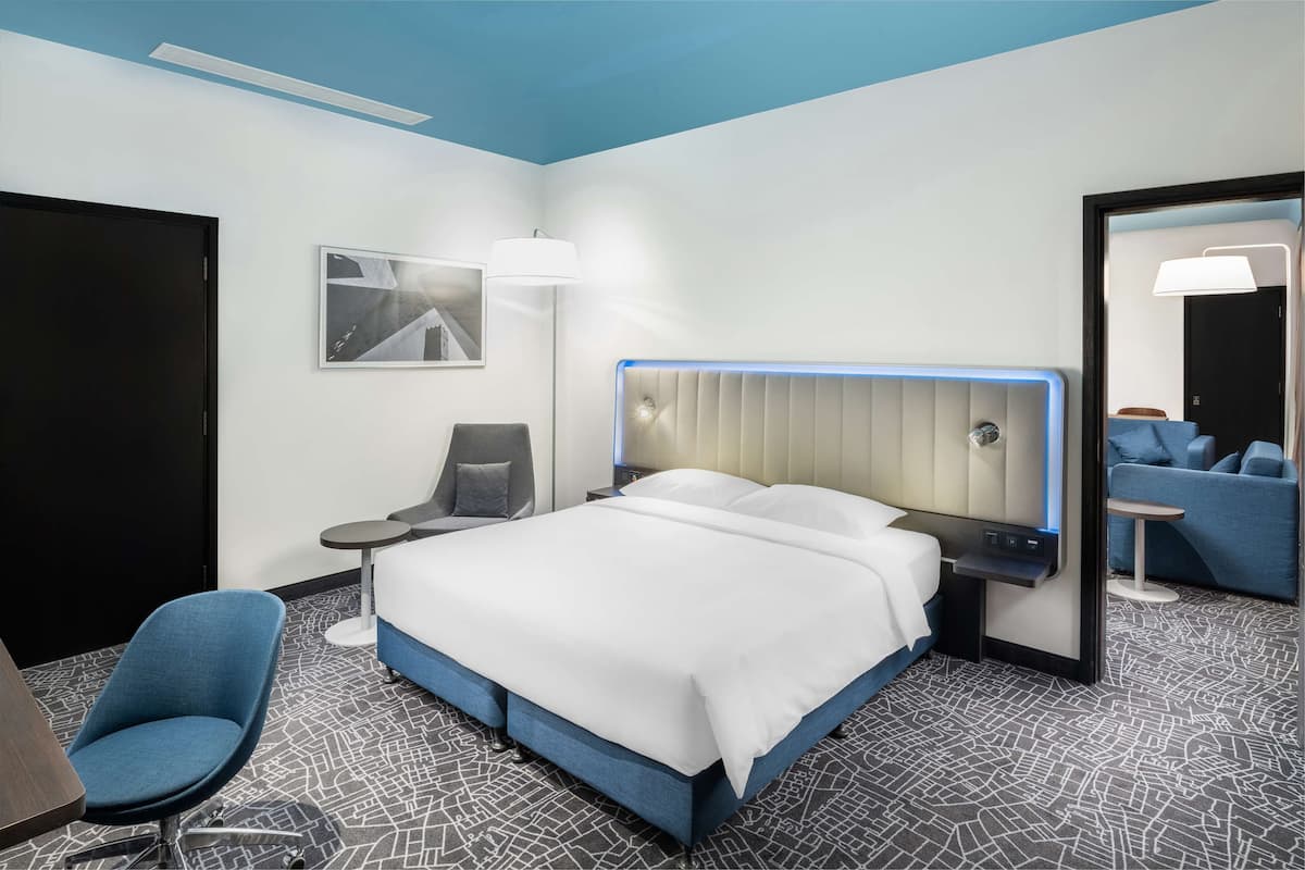 A modern hotel room with a large bed, a desk, a chair, a small table, and a mirror.