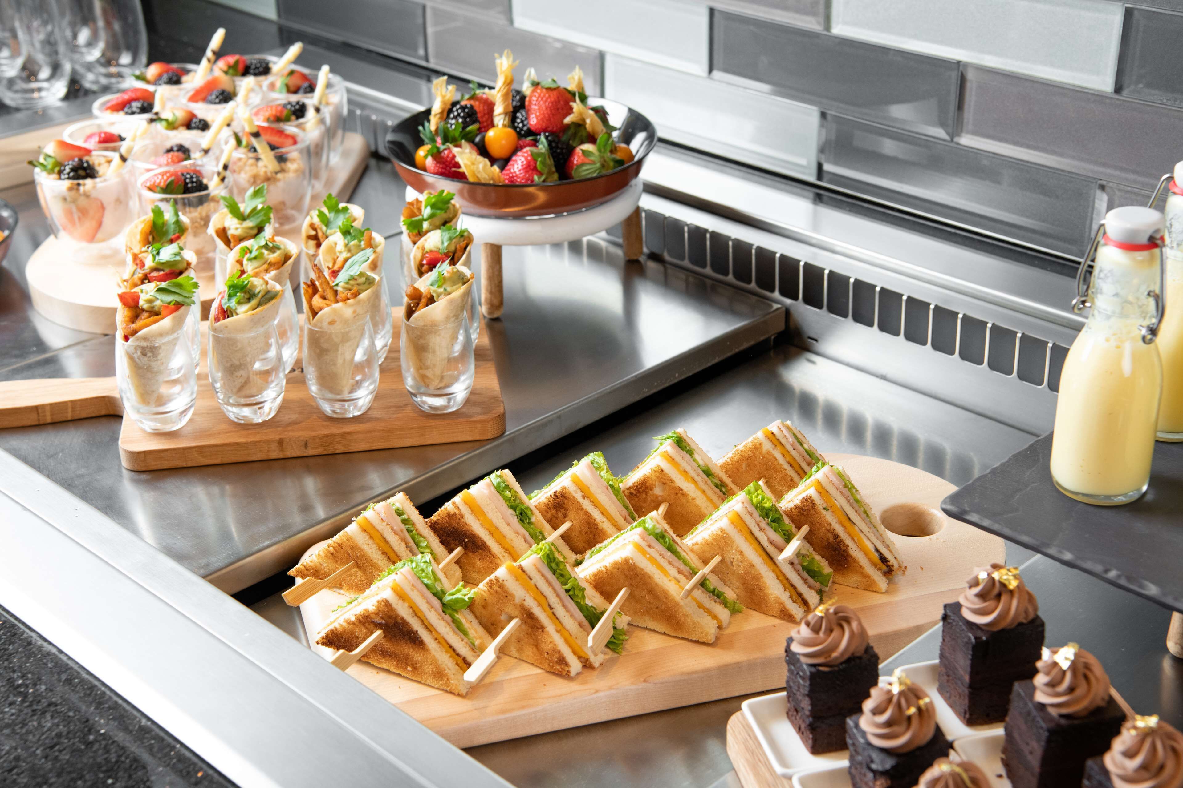 Un bufé con diferentes opciones de comida, como sándwiches, brochetas de fruta y postres.