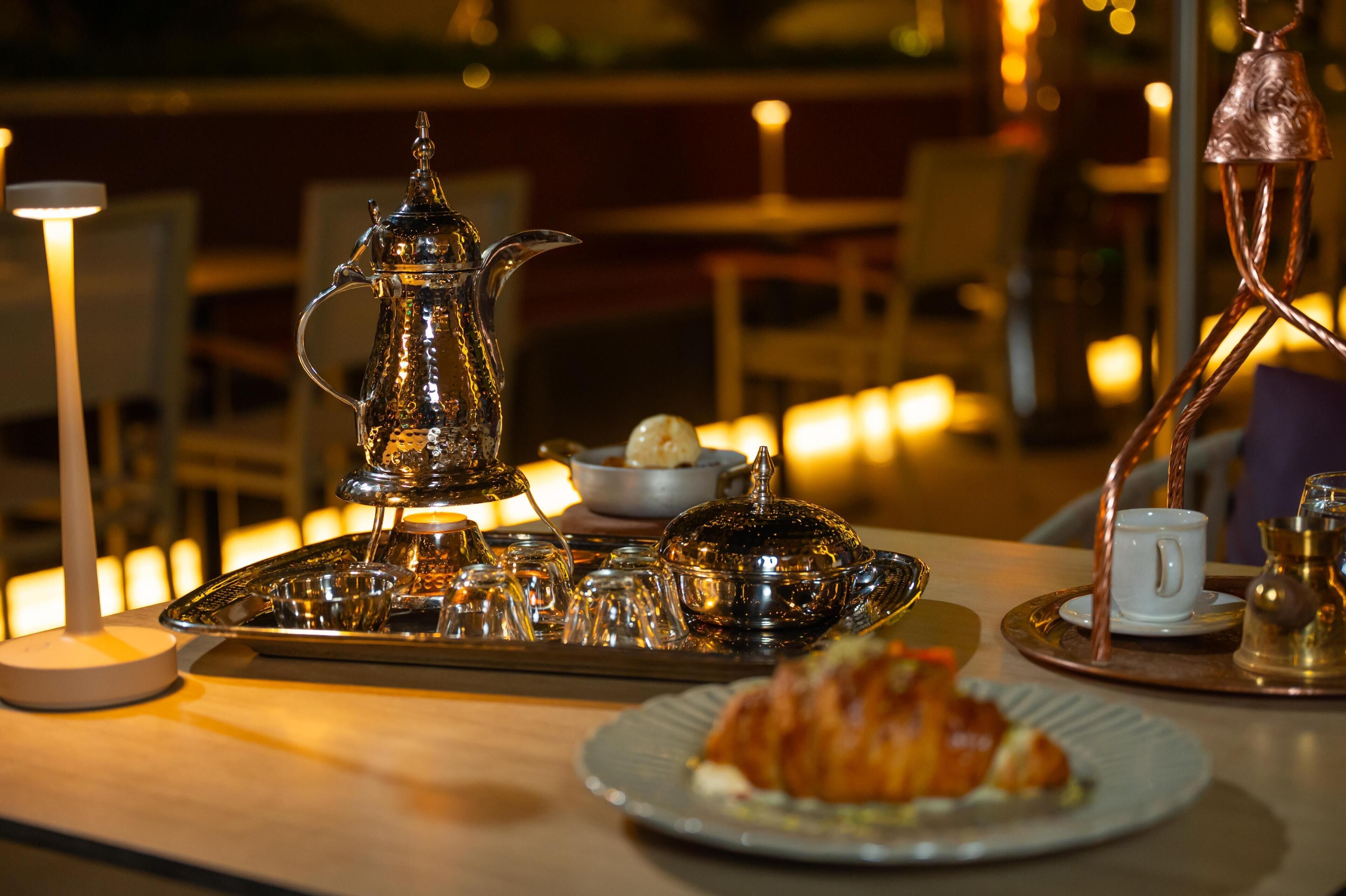 A table set with a teapot, cups, a tray, and a plate with a pastry.