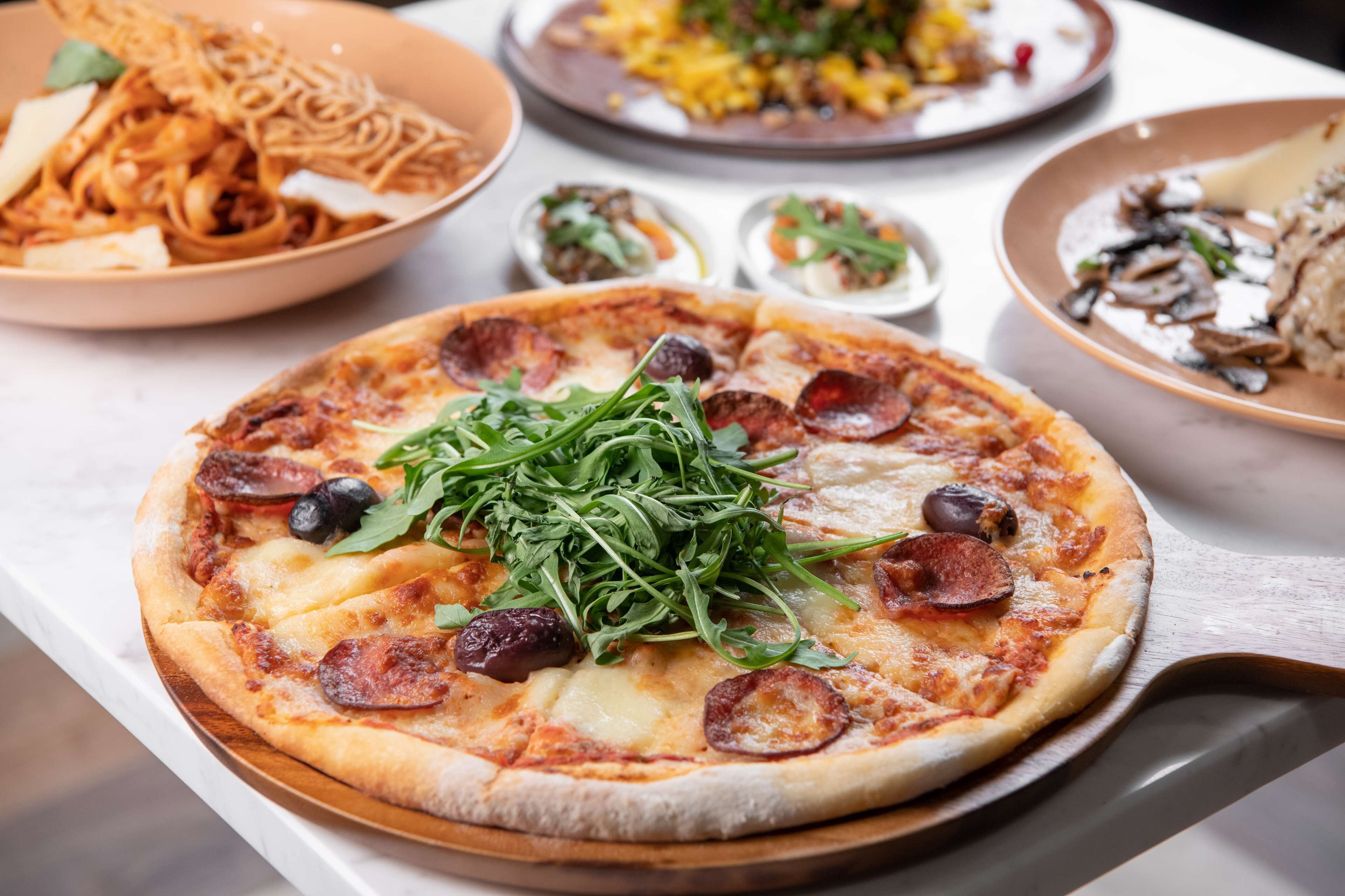A pizza with toppings and a wooden tray on a table.