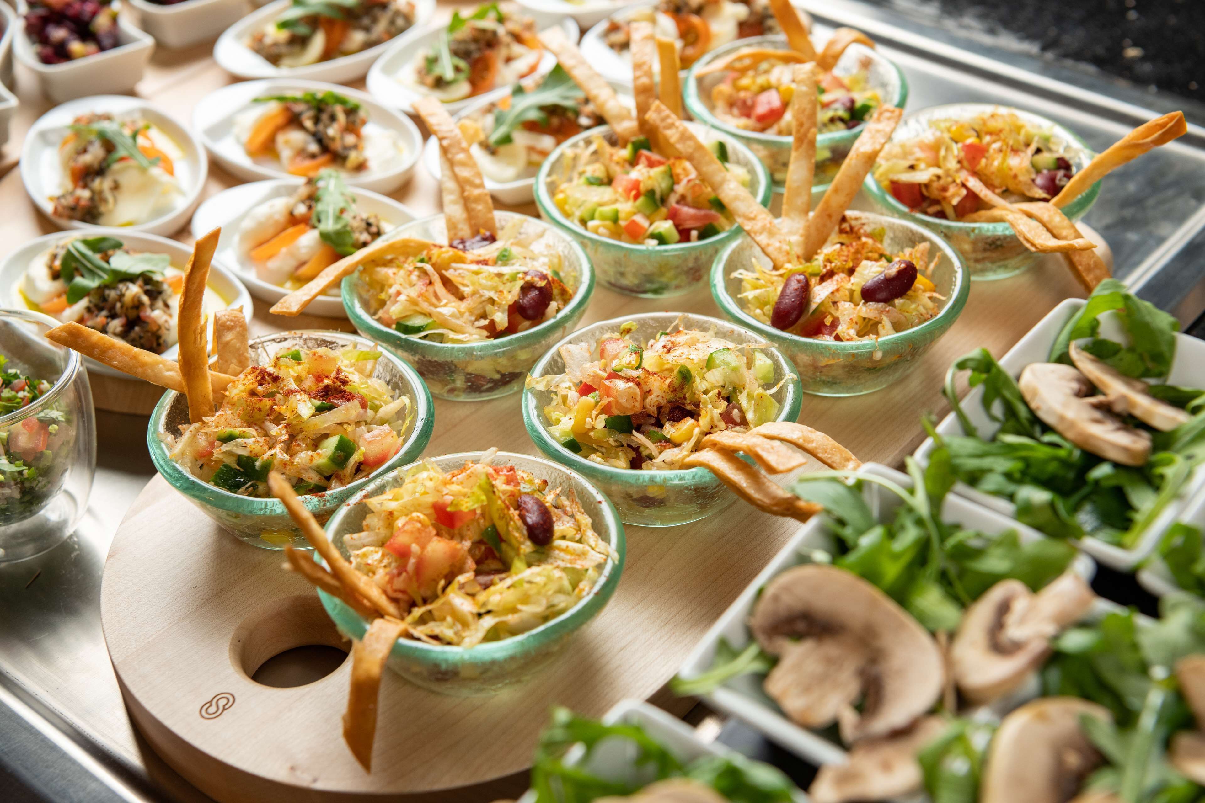 A variety of food items in glass bowls, including salads and appetizers, arranged on a wooden board.