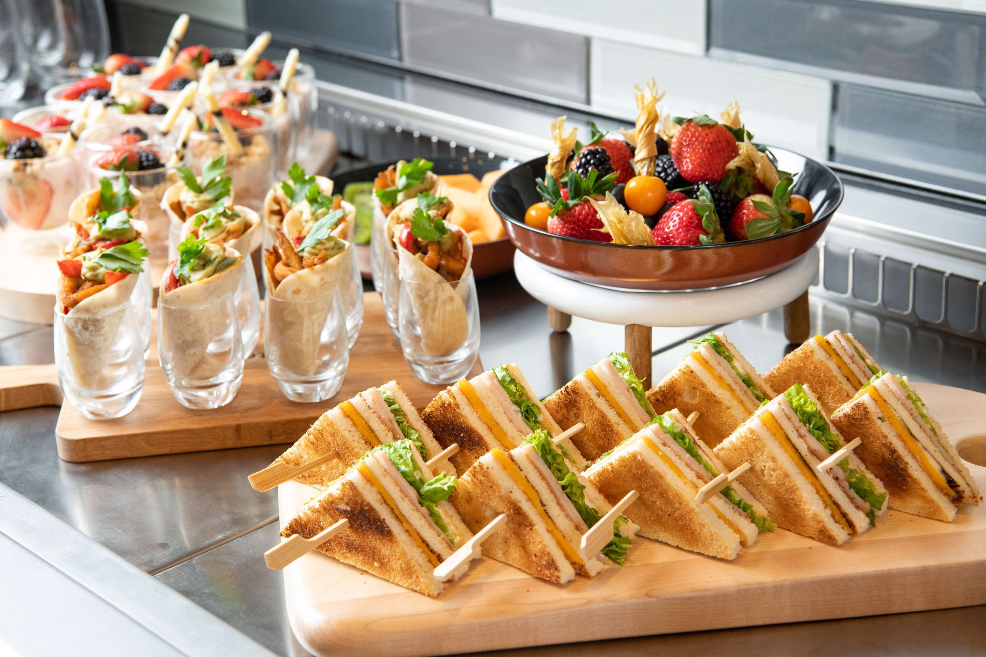 A buffet with various food items including sandwiches, fruit skewers, and a bowl of mixed berries.