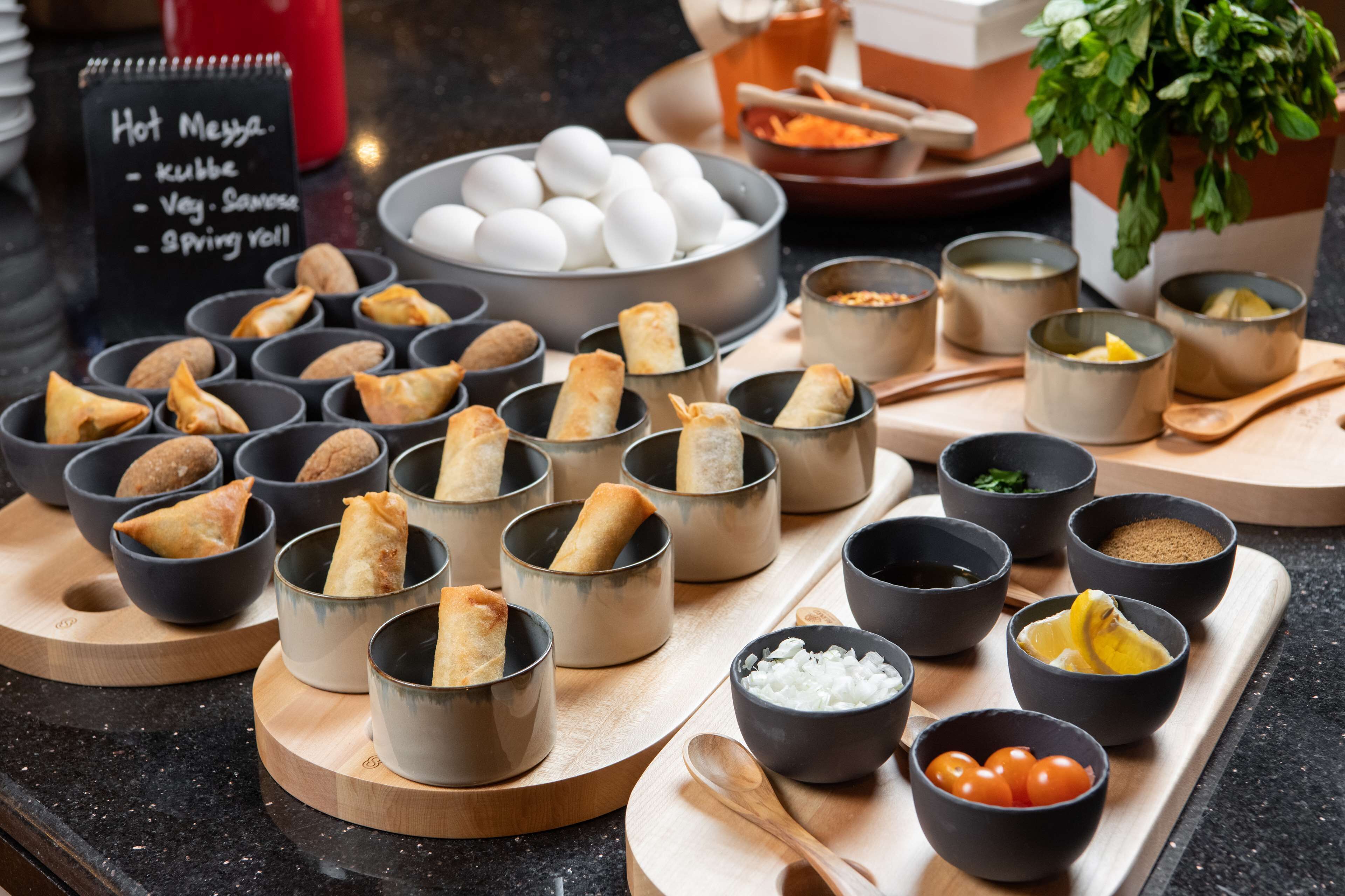 Variedad de alimentos, incluyendo samosas, huevos y salsas, sobre una tabla de madera.