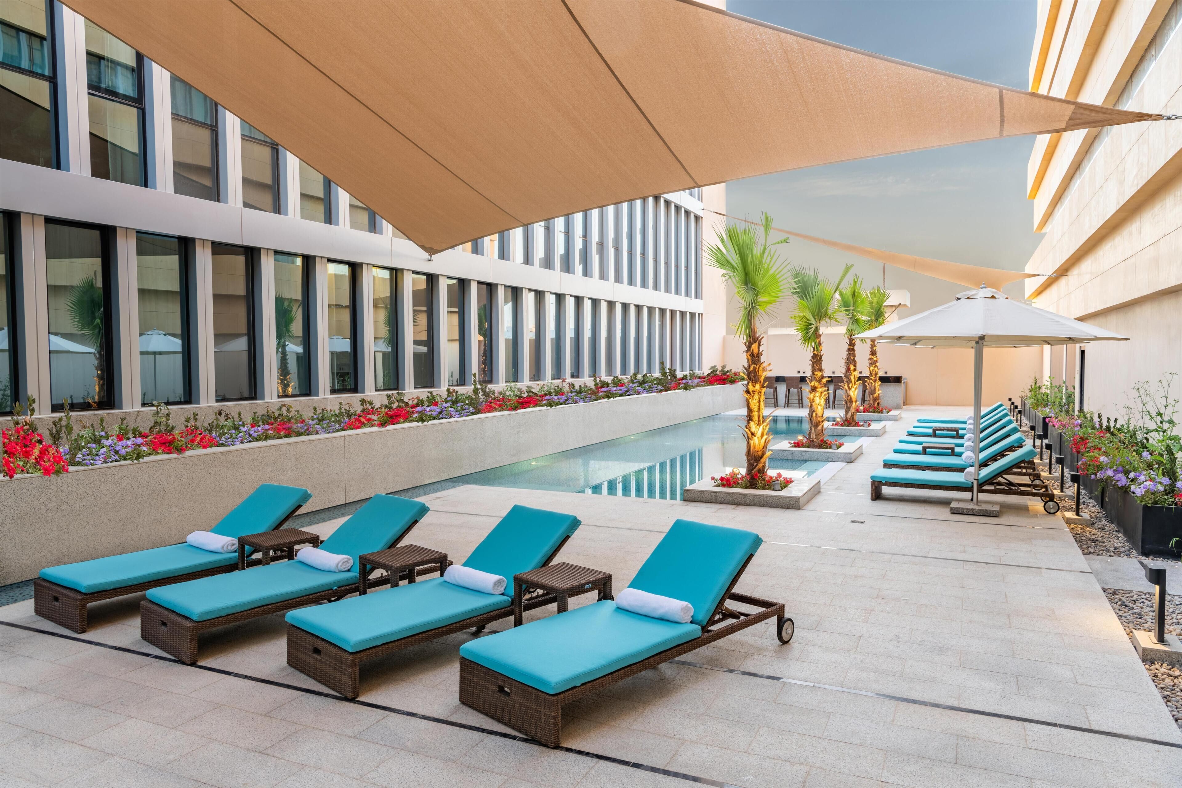 Zona de piscina con sillas de descanso, piscina y fachada de edificio.