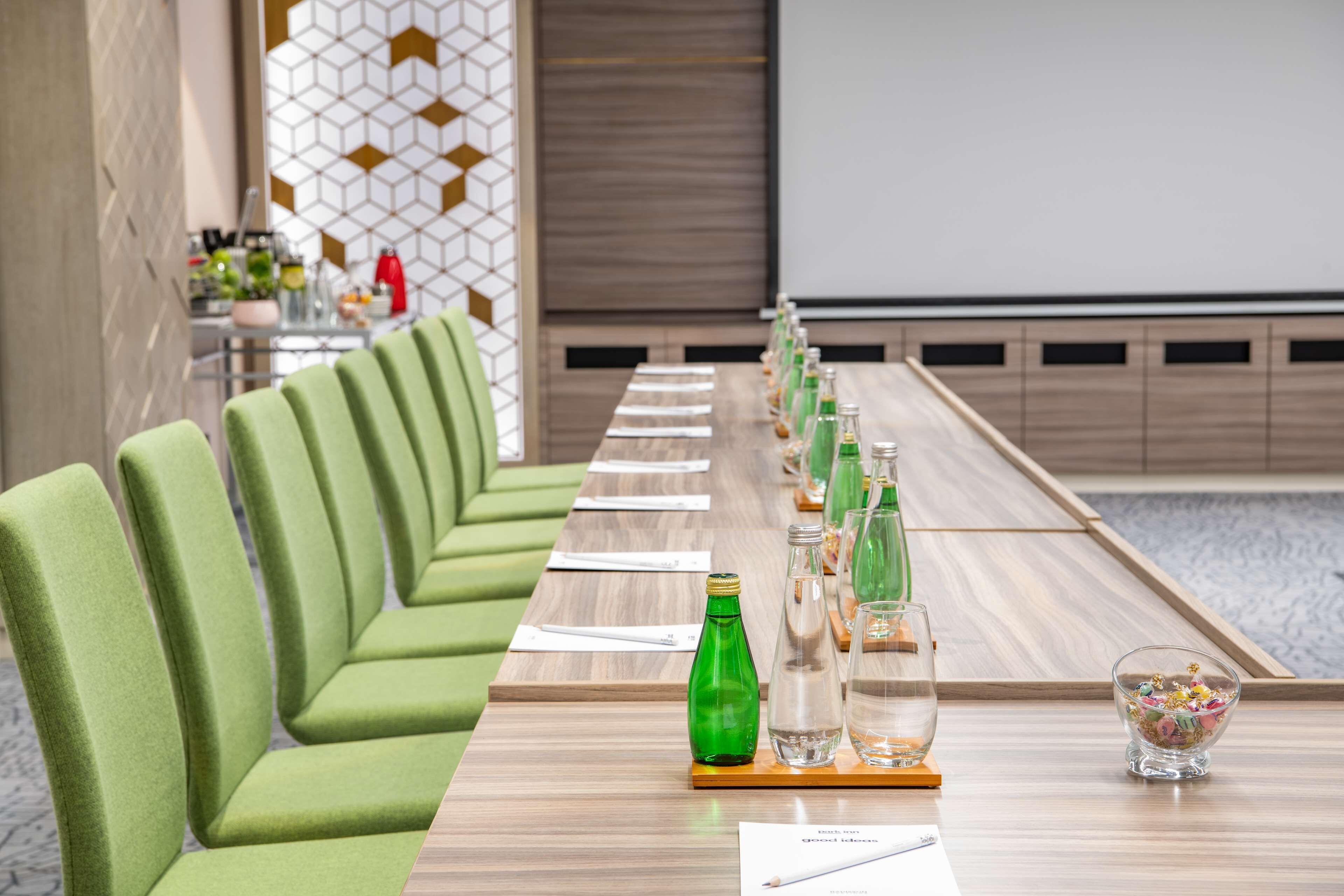 A conference room with green upholstered chairs, a long table with water bottles, glasses, and a bowl of snacks.