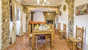 Un comedor con pared de piedra, una mesa de madera dispuesta para cuatro personas y una chimenea al fondo.